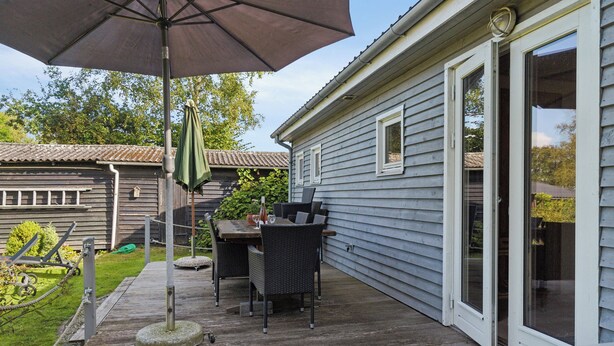 Eine Terrasse mit Tisch und Stühlen, einem großen Sonnenschirm und einem Haus mit einer Schiebetür.