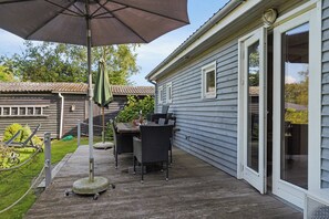 Un patio con mesa y sillas, un paraguas grande y una casa con puerta corrediza de vidrio.
