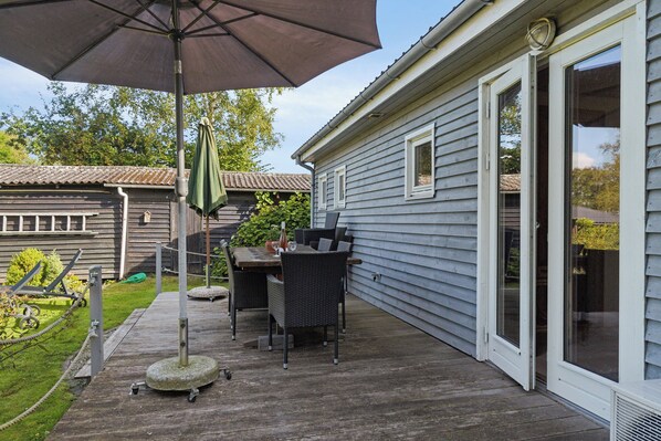 A patio with a table and chairs, a large umbrella, and a house with a sliding glass door.