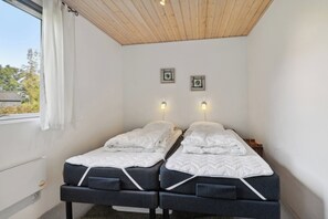 Una habitación con dos camas, una ventana con cortinas, techo de madera y luces fijadas a la pared.
