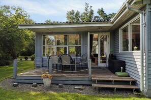 Ein kleines Haus mit Veranda, einem Esstisch mit Stühlen und einem Garten.