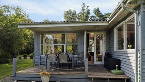 Un espace extérieur aménagé, abrité et doté de tables et de chaises, un petit jardin et un bâtiment avec de grandes fenêtres.
