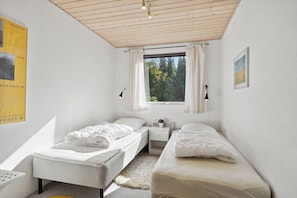 Ein Schlafzimmer mit zwei Betten, einem Fenster mit Vorhängen, einem Nachttisch mit Lampe und einem Poster an der Wand.