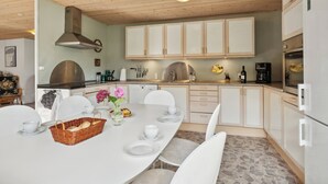 Une cuisine moderne avec des armoires blanches, une hotte en acier inoxydable et un coin repas doté d’une table blanche, mise pour quatre personnes.