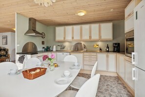 Cocina moderna con armarios blancos, extractor de acero inoxidable y comedor con una mesa blanca para cuatro.
