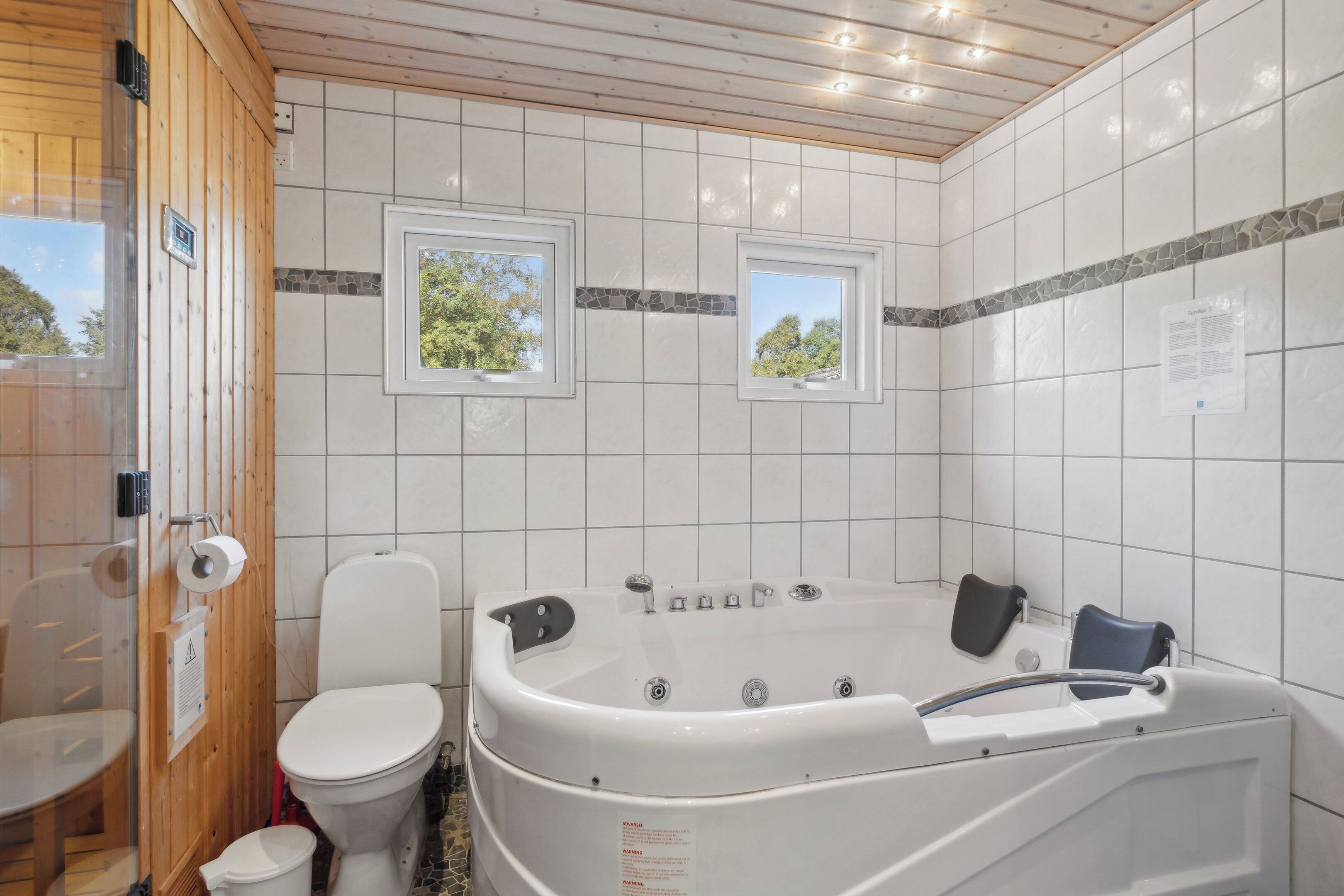 Une salle de bain avec des toilettes, une baignoire et deux fenêtres.