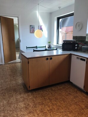 Une cuisine avec un îlot central en bois, une fenêtre, une horloge et un luminaire suspendu.