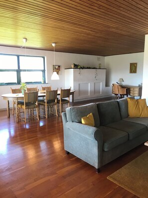 Un salon moderne avec un canapé gris, une table à manger en bois, des chaises et un coin cuisine doté d’un meuble blanc.