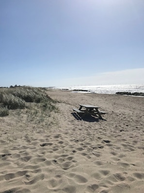 Une plage de sable avec une table de pique-nique en bois et des dunes en arrière-plan.