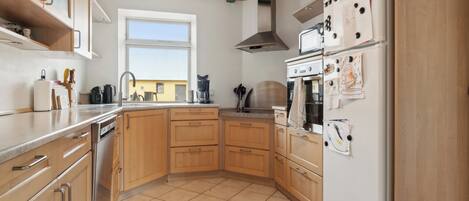 Cocina con gabinetes de madera, lavavajillas de acero inoxidable, horno doble y refrigerador con imanes.