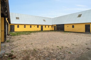 A courtyard with yellow buildings, a cobblestone ground, and a metal roof. - Idyllic country house with sea view and sunsets (Rønne)