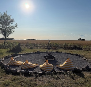 A circular outdoor seating area with striped cushions, a fire pit, and a view of a field and sky. - Idyllic country house with sea view and sunsets (Rønne)