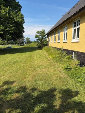 A yellow building with white windows, a grassy yard, and a tree. - Idyllic country house with sea view and sunsets (Rønne)