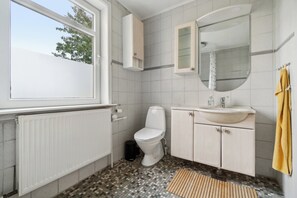 A bathroom with a toilet, sink, mirror, and window.