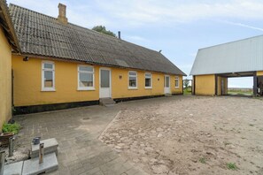 A yellow building with a tiled roof, a paved courtyard, and a separate building with a metal roof.
