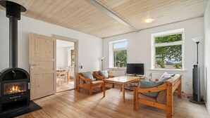 Ein gemütliches Zimmer mit Kamin, Holzmöbeln, einem Fernseher und großen Fenstern.