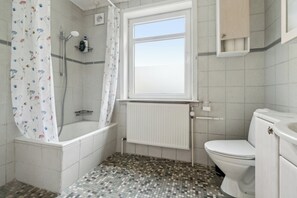 A bathroom with a shower, toilet, and a window.