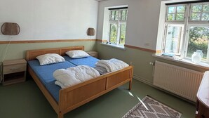Ein Schlafzimmer mit einem hölzernen Bett, einem Fenster, einer Heizung und einem gewebten Korb an der Wand.