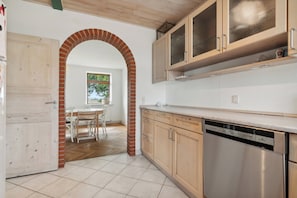 A kitchen with wooden cabinets, a dishwasher, and a brick archway leading to a dining area.