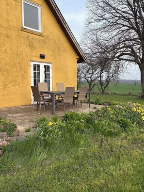A yellow house with a patio, outdoor seating, and a tree.