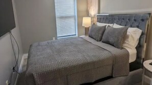Un dormitorio con cama, mesita de noche, lámpara y luz en el techo.