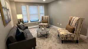 Una sala de estar con un sofá gris, un sillón estampado, una mesita de centro y una ventana con persianas.