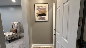 Un pasillo con suelo de madera, alfombra gris, un cuadro abstracto enmarcado en la pared y una puerta con marco blanco.