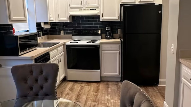 Una cocina moderna con armarios blancos, un refrigerador negro, una estufa y una mesa de comedor de vidrio con dos sillas.