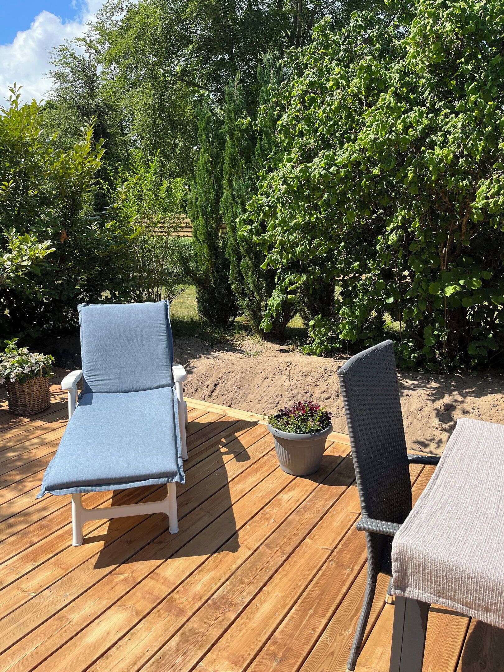 Una terraza de madera con dos sillas de descanso y una planta en maceta.
