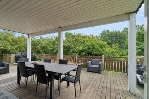 Une terrasse extérieure avec une table et des chaises, une plateforme en bois et une vue sur les arbres et une clôture.