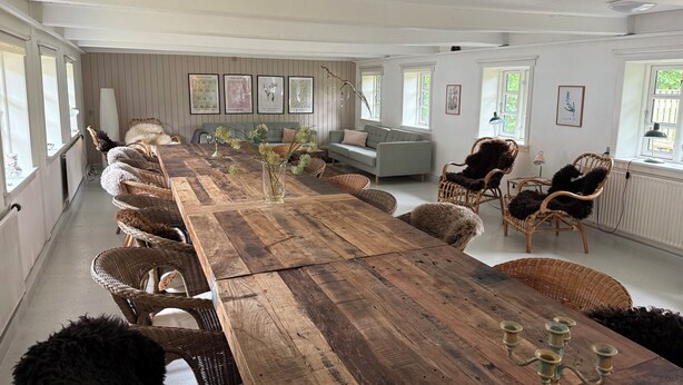 Une pièce spacieuse avec une longue table en bois, des chaises en osier, un canapé et des œuvres d’art encadrées accrochées aux murs.