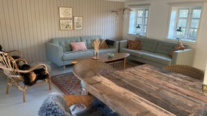 Un salon chaleureux avec une grande table en bois, deux canapés, des fauteuils en osier et un chien tout doux.