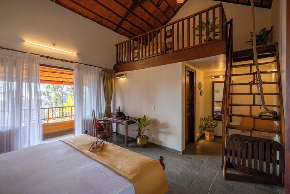 A bedroom with a bed, a desk, and a staircase to a loft area. - Amã Stays & Trails Alpenhof , Coorg (Madikeri)