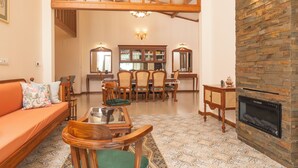 Ένα ευρύχωρο σαλόνι με ψηλό ταβάνι, τζάκι, τραπεζαρία με έπιπλα από ξύλο και ένα δάπεδο με διακοσμητικά σχέδια.