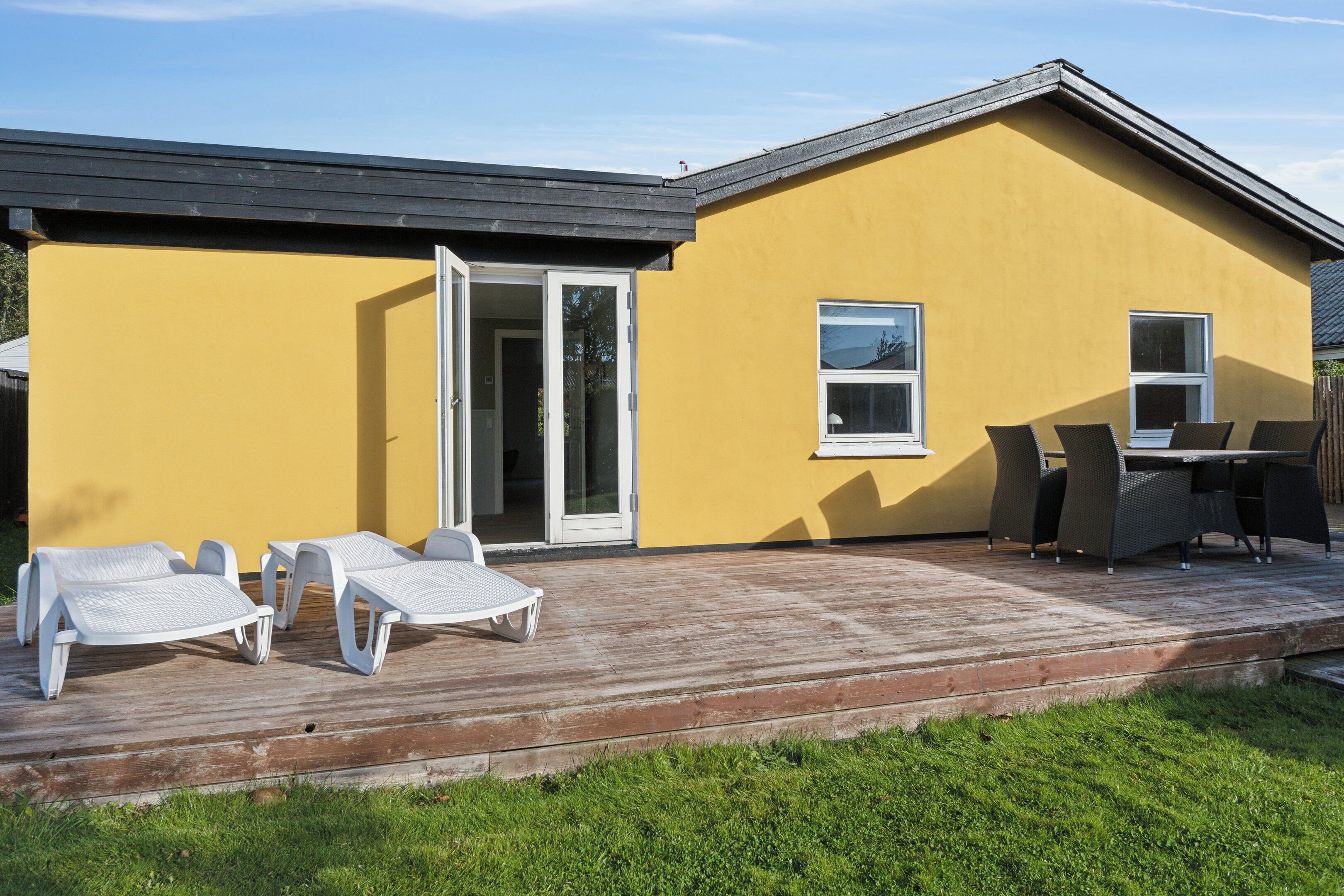 En gul bygning med terrasse, skydedør og et bord med stole.