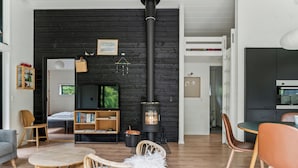 A cozy living room with a fireplace, wooden furniture, and a television. - Scenic summer house in Asserbo (Frederiksværk)