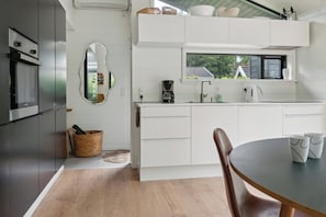 A modern kitchen with white cabinetry, a built-in oven, a coffee maker, and a window above the sink.