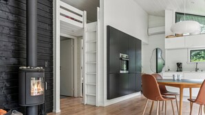 A modern kitchen with a built-in stove, white cabinetry, and a dining area with wooden chairs. - Scenic summer house in Asserbo (Frederiksværk)
