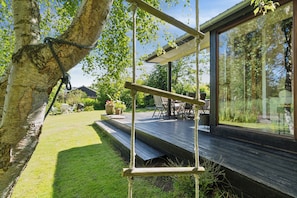 Een houten terras met een touwschommel, een glazen patio en uitzicht op de omliggende begroeiing.