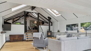 A spacious living area with a high ceiling, a fireplace, a sofa, a chair, and a staircase leading to an upper level.