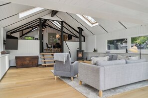 A spacious living area with a high ceiling, a staircase, a fireplace, and a large window.