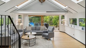 A modern living room with a high ceiling, skylights, a sofa set, a coffee table, and a view of the outdoors.
