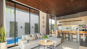 A modern living room with a sofa, a coffee table, and a view of a swimming pool. - Private Villa Ayra 9A 10min MelastiBeach (Ungasan)