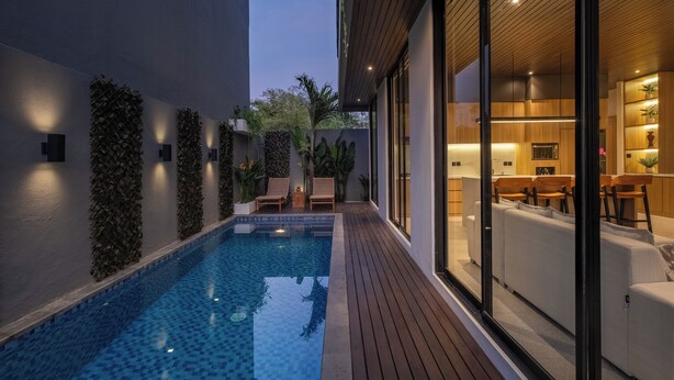 A modern pool area with a wooden deck, lounge chairs, and a glass-enclosed dining area. - Private Villa Ayra 9A 10min MelastiBeach (Ungasan)