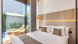 A modern bedroom with a large bed, a wooden headboard, a bedside lamp, and a view of a balcony with plants and a chair. - Private Villa Ayra 9A 10min MelastiBeach (Ungasan)