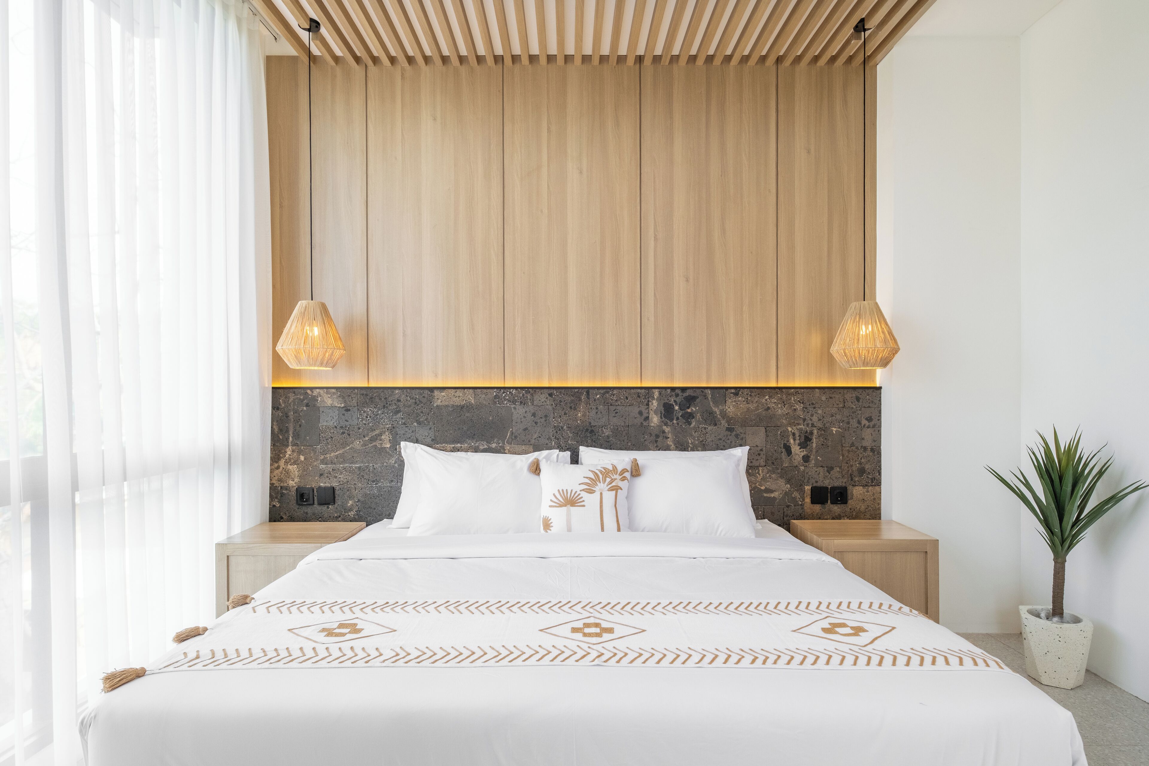 Un dormitorio moderno con techo de listones de madera, cabecera de piedra y cama con colcha estampada.
