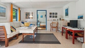 A modern living room with a sofa, dining table, TV, and artwork on the walls. - Cozy summer house on Bornholm (Nexø)