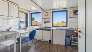 A kitchen with a dining area, a clock, and a view of the outdoors. - Cozy summer house on Bornholm (Nexø)
