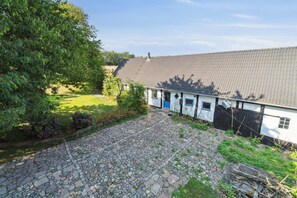 A stone-paved courtyard with a white building featuring a blue door and a satellite dish. - Cozy summer house on Bornholm (Nexø)