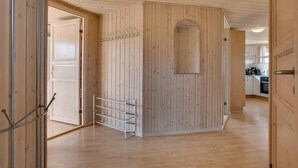 Ett rum med väggar beklädda med träpaneler, ett metallställ och en dörr som leder in till ett köksområde.